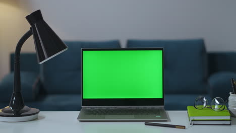 Arbeitstisch-Im-Home-Office-Mit-Laptop,-Lampe,-Buch-Und-Brille,-Greenscreen-Für-Chroma-Key-Technologie,-Zoom-Aufnahme,-Mann-Schaltet-Tischlampe-Aus